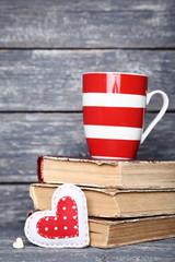 Obraz premium Fabric heart with cup and old books on wooden table