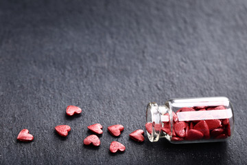 Red heart shaped sprinkles in glass bottle on black background