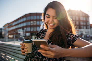 Smiling Asian university student sitting on campus sending a text