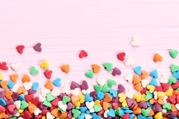 Fototapeta na wymiar Colorful heart shaped sprinkles on pink wooden table