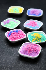 Colorful holi powder in bowls on black wooden table