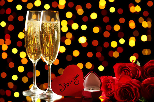 Champagne glasses with red roses and silver ring on lights background