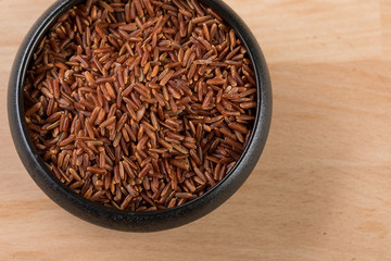 Rotschaliger roher Roter Jasmin Reis in schwarzer Schale auf Holz Hintergrund und ist eine Spezialität aus Kambodscha Asien