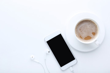 Fototapeta na wymiar Smartphone with earphones and cup of coffee on white background