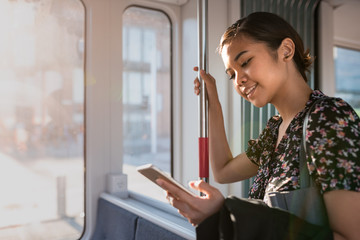 Smiling Asian businesswoman riding on a train using her cellphone