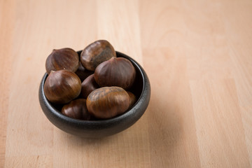 Maronen Esskastanien in schwarzer Schale auf Holz Hintergrund 