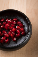 Rote Granatapfel Kerne in schwarzer Porzellan Schale auf Holz Hintergrund