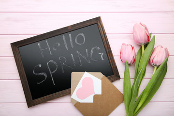 Inscription Hello Spring with envelope and tulips on pink wooden table