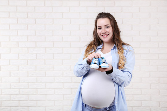 Beautiful Pregnant Woman With Baby Shoes On Brick Wall Background