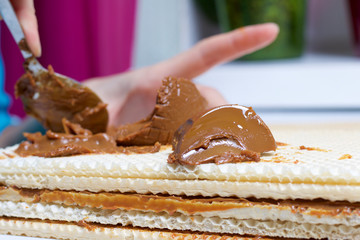 Cooking waffle cake. A woman smears wafer cake layers with boiled condensed milk. On the table is an open can of boiled condensed milk.