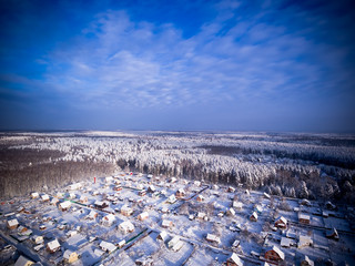 Village in forest. Winter aerial view. Blue cloudy sky.
