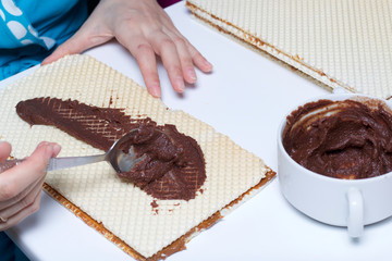 Cooking waffle cake. A woman lubricates the wafer cakes with a mixture of cocoa and butter. Nearby are wafer cake layers smeared with boiled condensed milk.