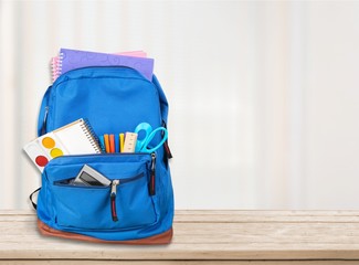 Open blue school backpack on wooden table in classroom