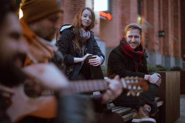 A company of friends on the bench plays the guitar.