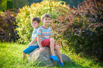 Naklejka na ściany i meble Two boys sitting on a rock in the park on sunny warn evening or day. Season, children, lifestyle concept