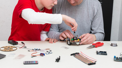 A teenager boy with his dad teacher collects a handmade robot working on the arduino platform. STEM education for children and teenagers, robotics and electronics. DIY. AI. STEAM.