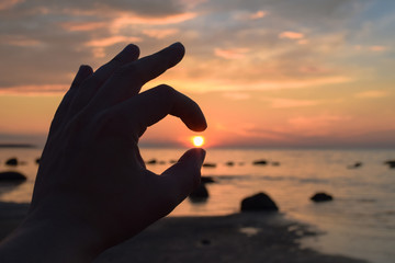 silhouette of arm holding sun on the beach