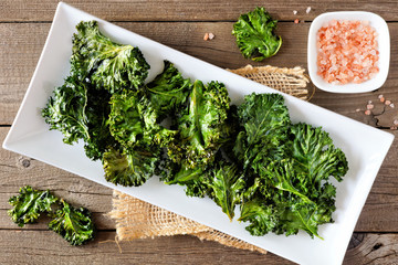 Plate of healthy organic kale chips, top view on rustic a wood background - obrazy, fototapety, plakaty