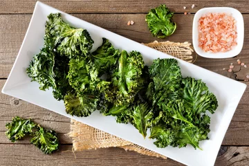 Poster Plate of healthy organic kale chips, top view on rustic a wood background © Jenifoto