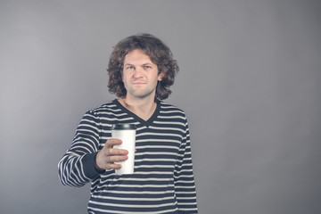Portrait of happy handsome dark haired curly man in striped sweater with paper cup of morning coffee isolated on grey background. Good morning with tea. Takeaway coffee. Time for break. Space for text