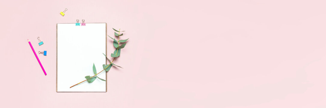 Flat lay clipboard with blank paper, colour pencils, clips, eucalyptus branches on pink background. Top view female office workspace minimal mock up template concept copy space Feminine floral desktop
