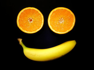 Fruit smile. Simple fruit face made of banana and two orange halves on black background