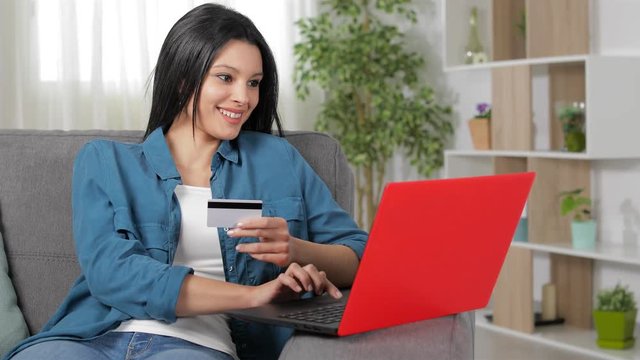 Happy woman paying on line with credit card and laptop sitting on a couch at home