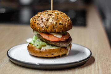 Tasty burger with grilled beef, lettuce and mayonnaise served on ceramic plate on regular bright kitchen, close up, with copyspace