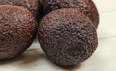 Detail of ripe whole brown avocado, rough skin visible, more avocados on white boards in background.