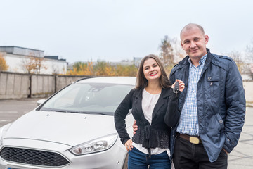 Smiling couple posing near new car with keys