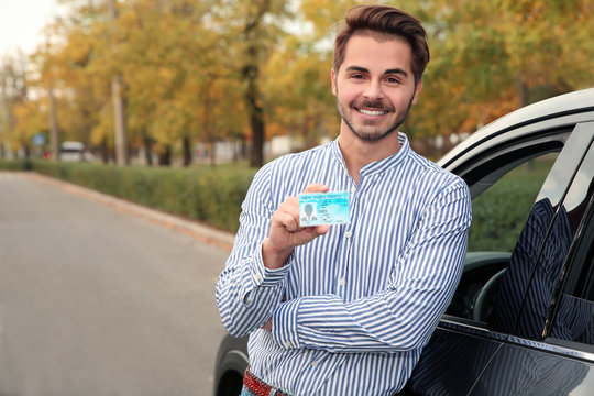 Young man holding driving license near open car. Space for text