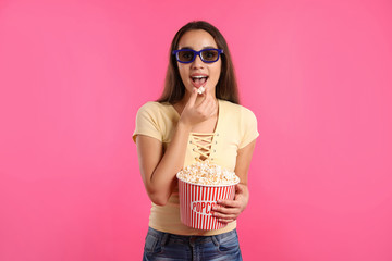 Woman with 3D glasses and popcorn during cinema show on color background