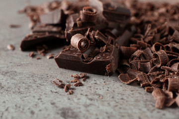 Curls and pieces of tasty chocolate on gray background, closeup