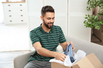 Young man opening parcel on sofa at home