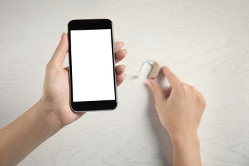 Woman with smartphone and hearing aid on light background, top view. Space for text