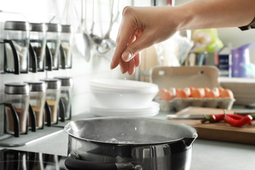 Woman salting boiling water in pot on stove, closeup