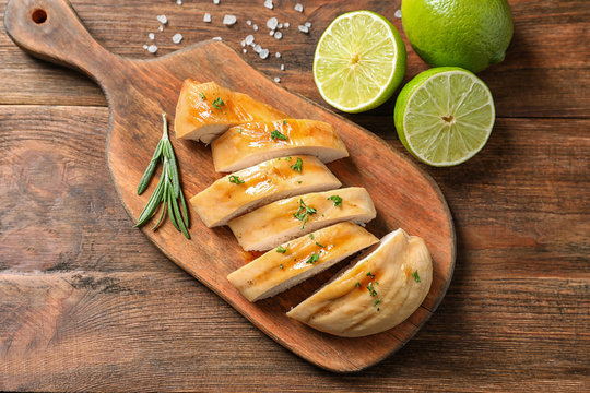 Board with fried chicken breast and limes on wooden background, top view