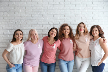 Group of women with silk ribbons near brick wall. Breast cancer awareness concept