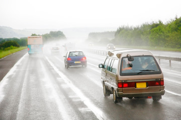 Obraz na płótnie Canvas Traffics on a rainy wet highway in fog water spray