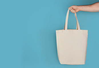 Man holding cotton shopping eco bag on color background. Mockup for design