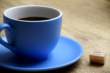 Coffee in a large blue cup on wooden table with a sign next to it saying yes please. Concept image of coffee addiction or coffee lover.