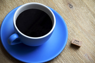 Cup of coffee on wooden table with a sign next to it saying yes please