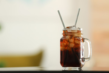 Mason jar of cola with ice on table against blurred background. Space for text