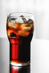 Glass of cola with ice on table against blurred background