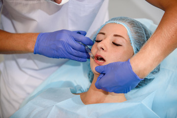 girl do plastic operation in medical clinic; doctor does lip augmentation surgery; injecting operation on lips