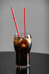 Glass of cola with ice on table against grey background