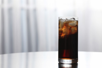 Glass of cola with ice on table against blurred background. Space for text
