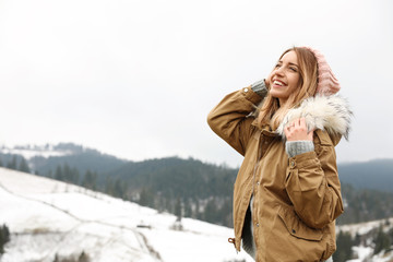 Fototapeta na wymiar Young woman in warm clothes near snowy hill, space for text. Winter vacation