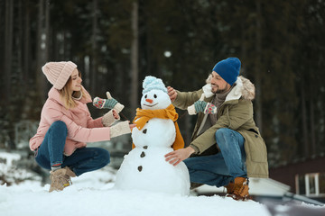 Couple making snowman outdoors. Winter vacation