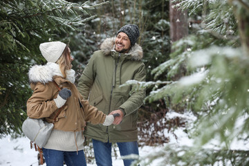 Fototapeta na wymiar Couple in conifer forest on snowy day. Winter vacation